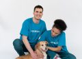 A diverse group of volunteers posing happily with a cute dog in a bright studio setting.
