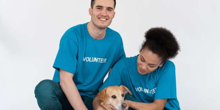 A diverse group of volunteers posing happily with a cute dog in a bright studio setting.